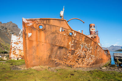 Low angle view of old damaged boat on field against blue sky during sunny day