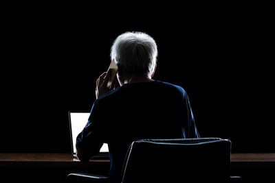 Rear view of person using mobile phone and laptop against black background