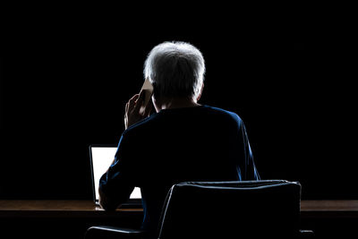 Rear view of woman sitting on chair against black background