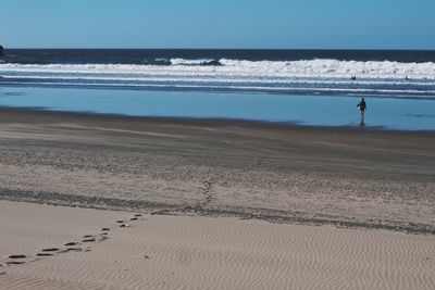 Rear view of woman walking at beach against sky