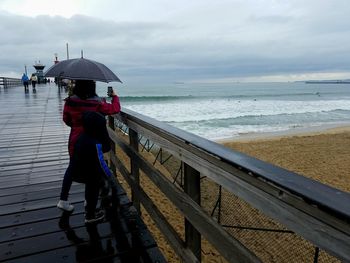 Rear view of woman standing on pier at beach during rainy season