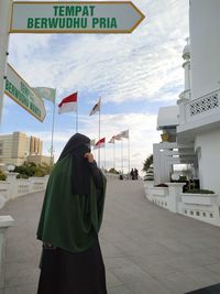 Rear view of woman standing on cross against sky