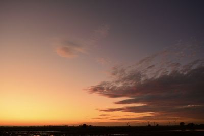 Scenic view of dramatic sky over silhouette field during sunset