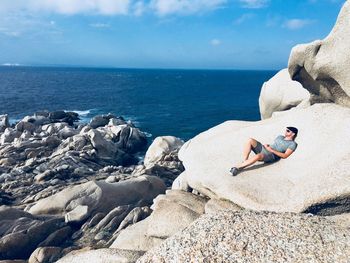 Man on rock by sea against sky