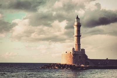 View of lighthouse by sea against cloudy sky