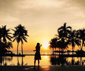 Silhouette woman standing by swimming pool at beach during sunset