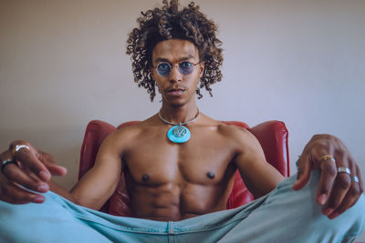 Portrait of shirtless young man wearing sunglasses against on a red couch. 