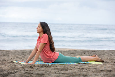 Peaceful hispanic lady practicing bhujangasana yoga pose on sandy seashore
