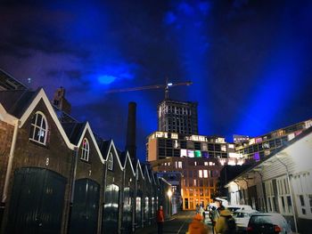 Illuminated street amidst buildings against sky at night