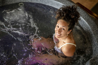 Mixed race woman smiling while relaxing in a hot tub.