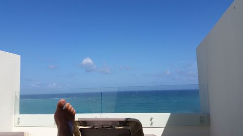 Close-up of hand against sea against clear blue sky