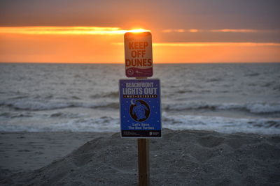 Information sign on beach against sky during sunset