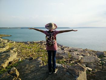 Rear view of boy standing on rock by sea against sky
