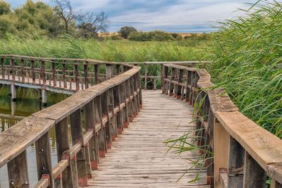 Wooden footbridge on field against sky