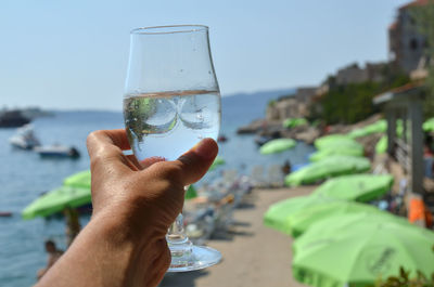 Midsection of person holding drink against sea
