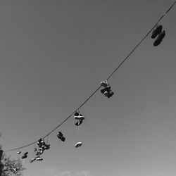 Low angle view of shoes hanging on cable against clear sky