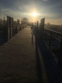 Footpath by railing in city against sky during sunset