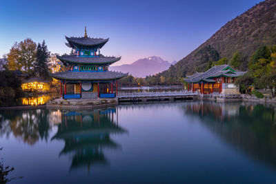 Gazebo in lake by building against sky at dusk