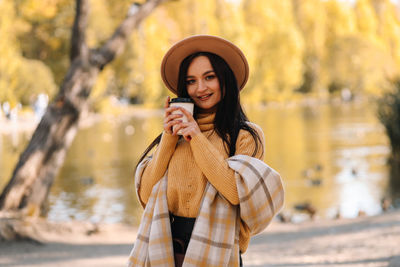 Beautiful smiling girl in casual clothes drinking coffee walking in nature in autumn outdoor