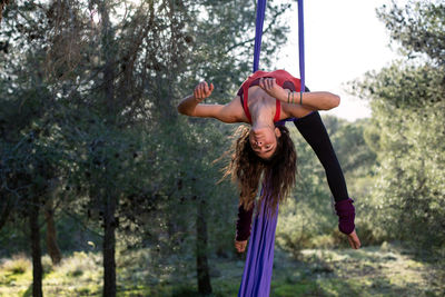 Young girl acrobat. practicing aerial silks. woman doing circus stunts with clothes in the forest. candy cane trick pose.