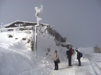 Rear view of people on snow covered mountain against sky