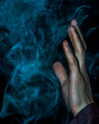 Close-up of cropped hand by smoke against black background