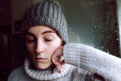 Melancholic young woman looking through window