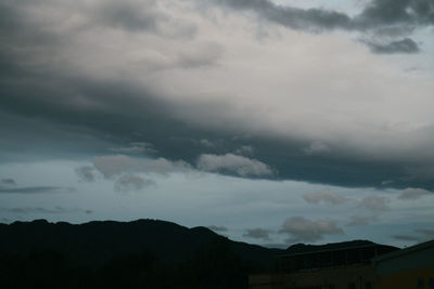 Low angle view of storm clouds over silhouette mountain