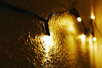 Close-up of illuminated lamp against wall at night