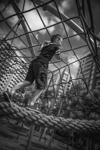 Low angle view of boy climbing on rope in playground