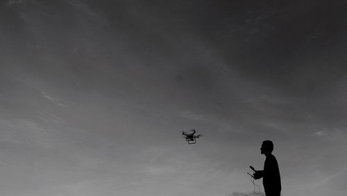 Low angle view of man flying drone against sky