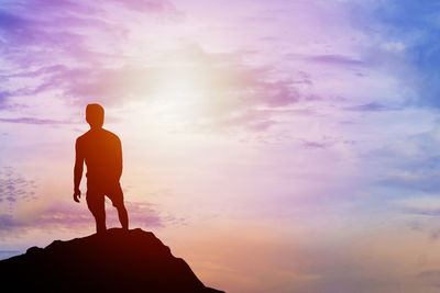 Silhouette man standing on rock formation against sky during sunset