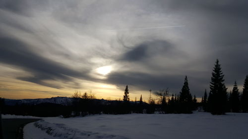 Snow covered field against cloudy sky