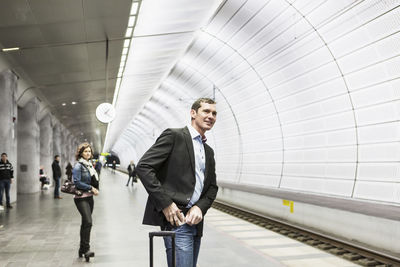 Businessman putting mobile phone in pocket while standing at railroad station platform