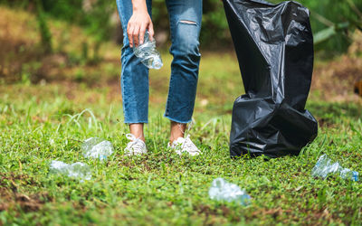 A female activist picking up garbage plastic bottles into a plastic bag in the park for recycling