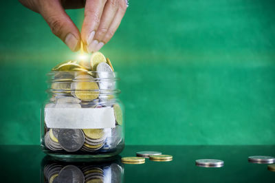 Cropped hand of person putting coin in jar on table