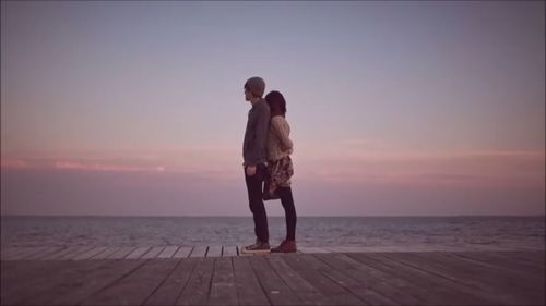 Couple standing on sea against sky during sunset