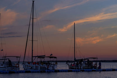 Sailboats moored at harbor during sunset