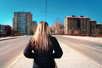 Rear view of woman on road in city against sky