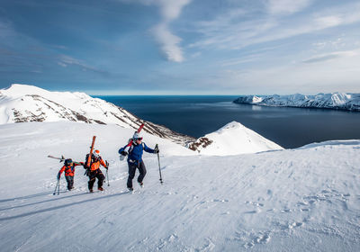 Men hiking uphill with skies in iceland with water in background