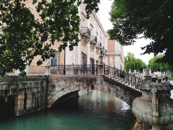 Arch bridge over river by buildings against sky