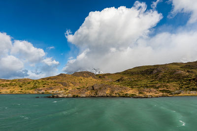 Scenic view of sea by mountain against sky