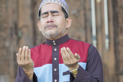 Close-up of mature man praying while sitting at mosque