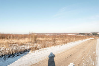 Road passing through field against clear sky