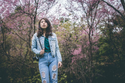 Beautiful young woman looking away while standing against pink flowering tree