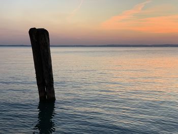Wooden posts in sea against sky during sunset