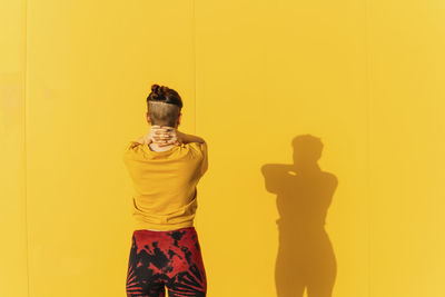 Woman with hands on neck standing in front of yellow wall