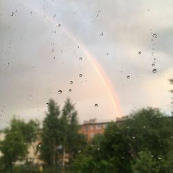 Close-up of wet glass window against rainbow