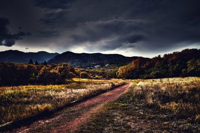 Dirt road along countryside landscape against cloudy sky