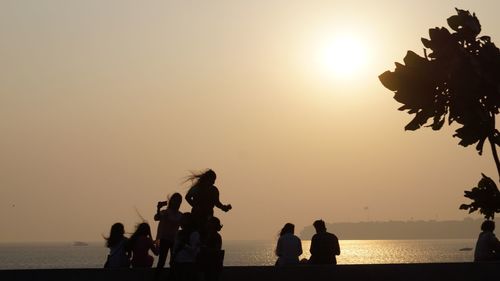 Silhouette people standing on beach against sky during sunset